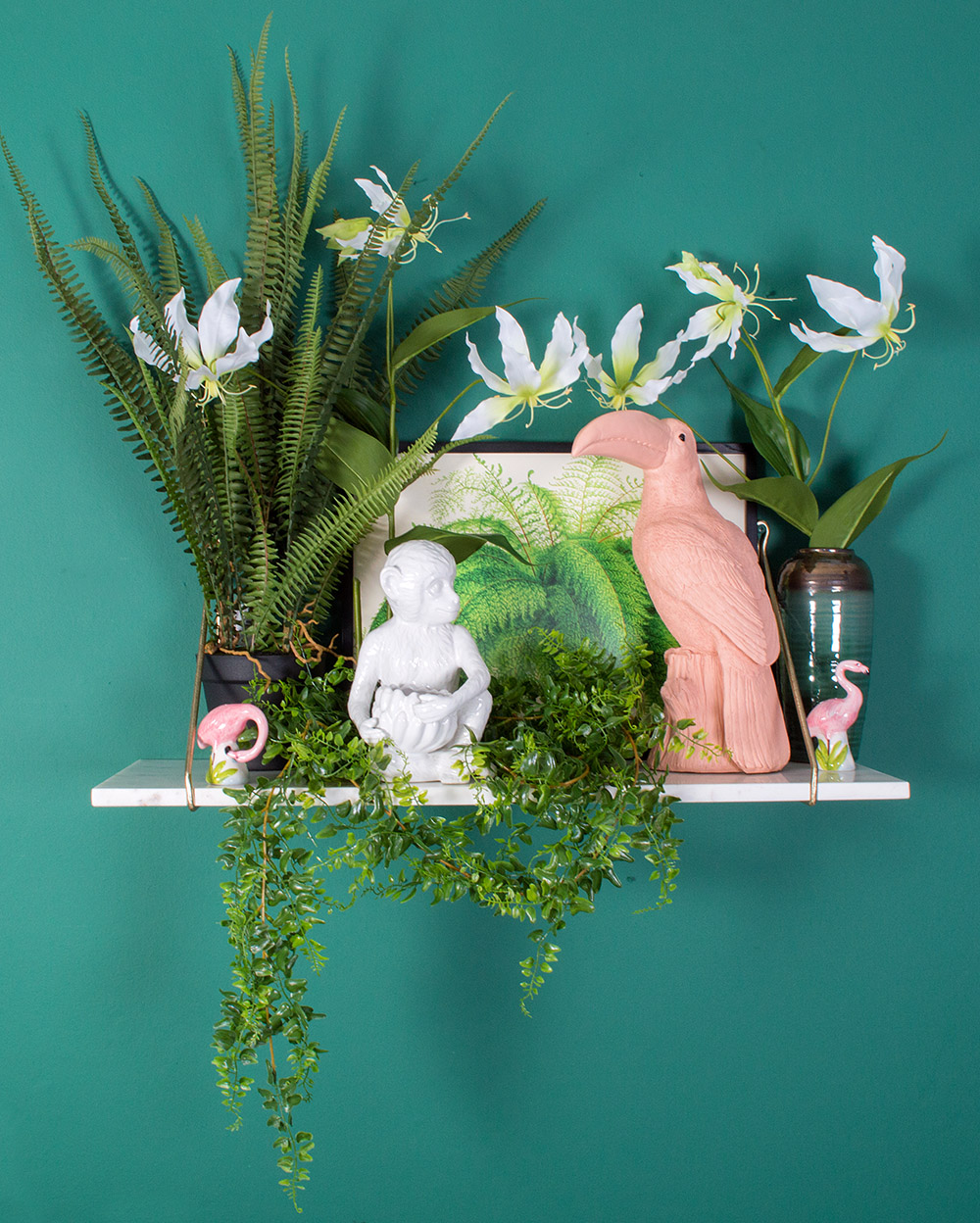 A bit of tropical and a bit of whimsy all snuggled up together creates a white marble shelf that has the look of a Victorian collector’s display. Curios from around the world come together for a touch of the exotic, with a pink toucan money box, a cheeky monkey plant pot and some flamingos for a laugh. Lots of lush faux greenery and lily flowers completes the look.