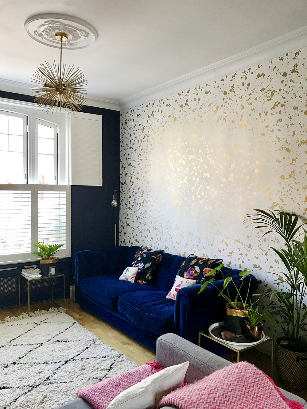 After: Living room transformation. Colourful space with lavish gold details, featuring Gold Drip wallpaper by Jonathan Adler and a luxurious blue velvet sofa.