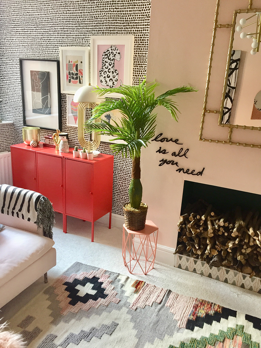 An eclectic living room with pink walls and monochrome wallpaper. 