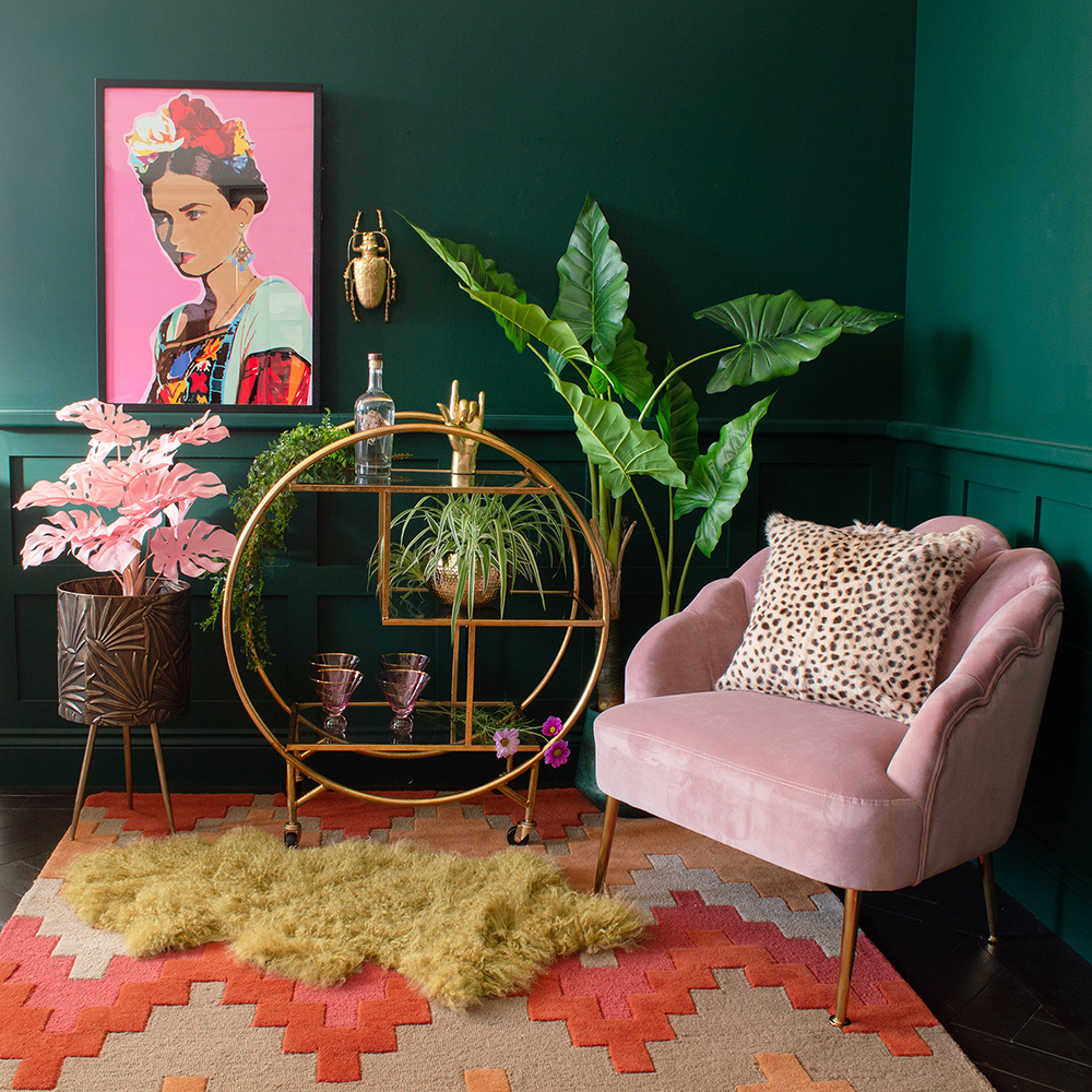 Cool living room decor with green walls, gold drinks trolley and pink velvet armchair.