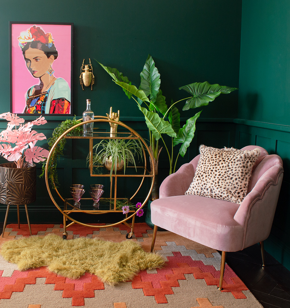Cool living room decor with green walls, gold drinks trolley and pink velvet armchair.