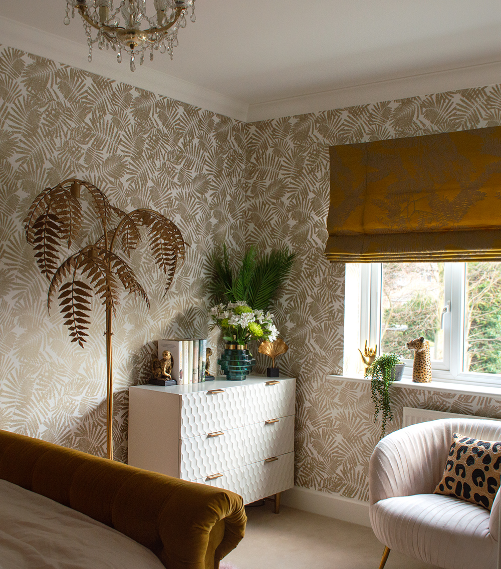 Feminine bedroom decor with patterned gold tropical wallpaper.