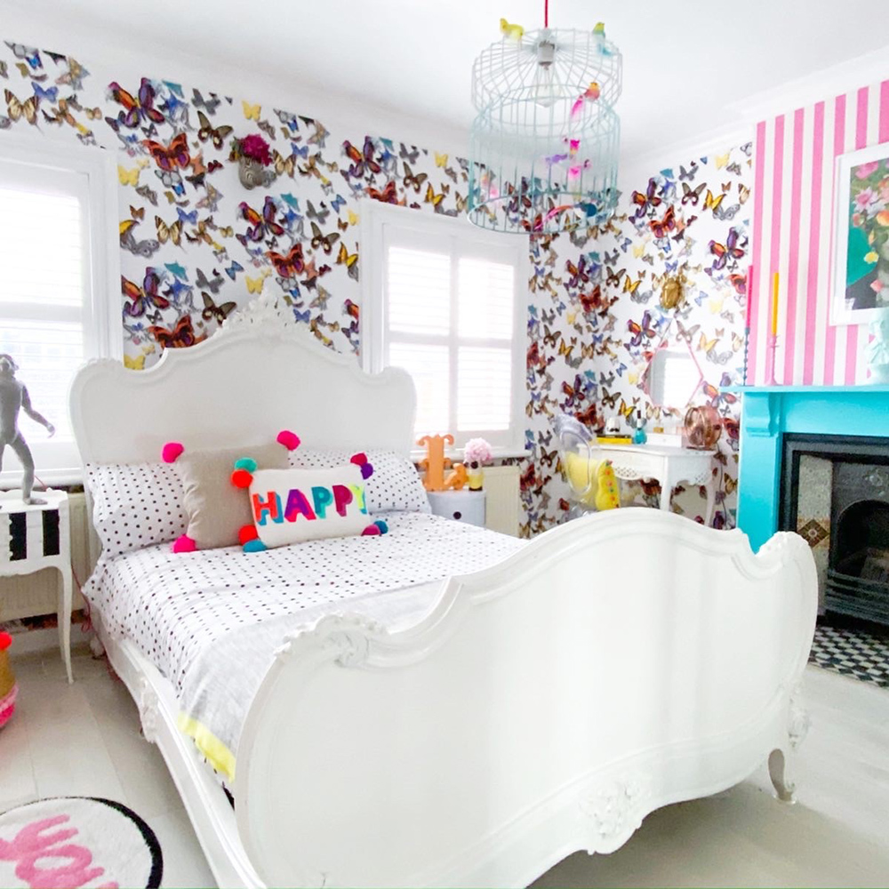 Quirky bedroom decor with butterfly wallpaper and neon pom pom cushions