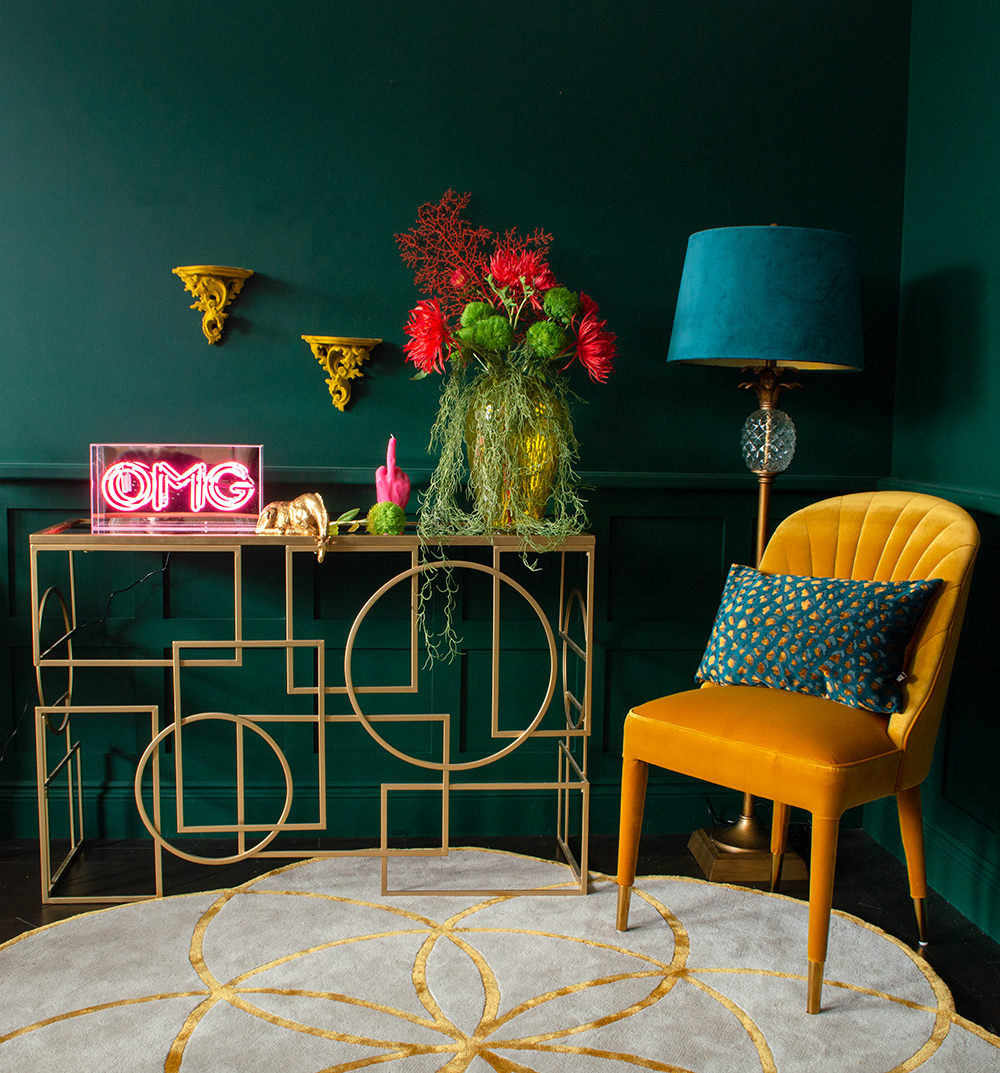 Gold console table styled with pink neon, colourful faux flowers and mustard yellow velvet chair.