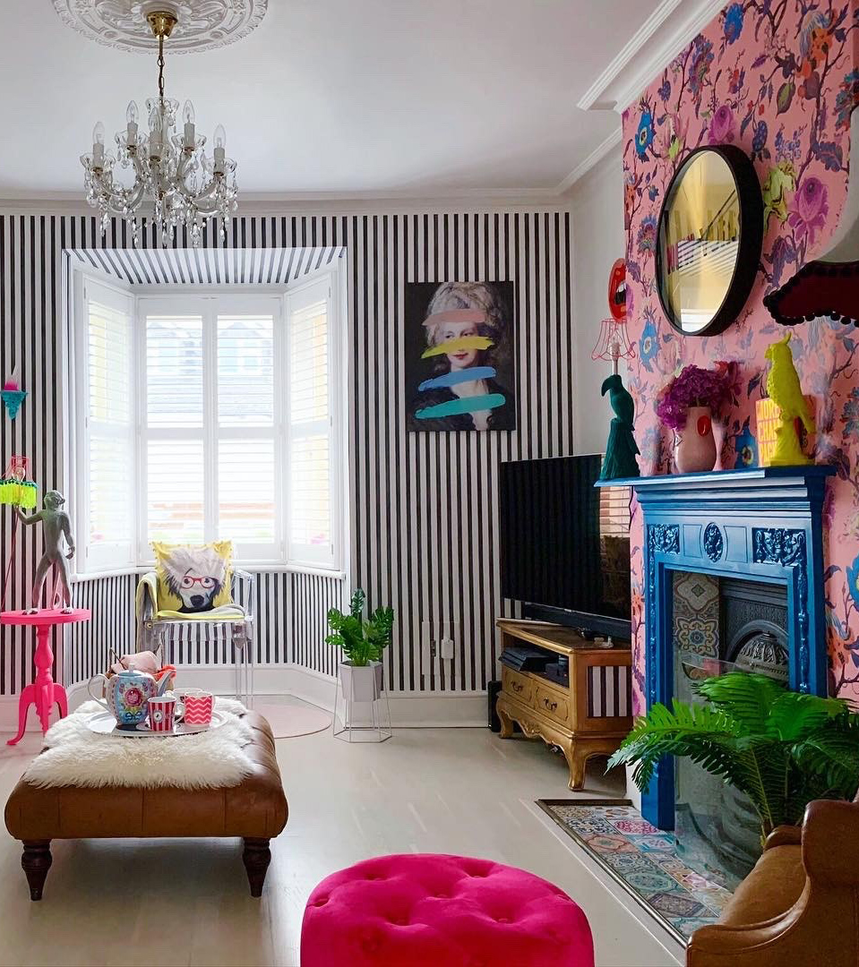 Cool and colourful living room decor with bright pops of pink, monochrome striped wallpaper, pink floral wallpaper and bright blue fireplace!