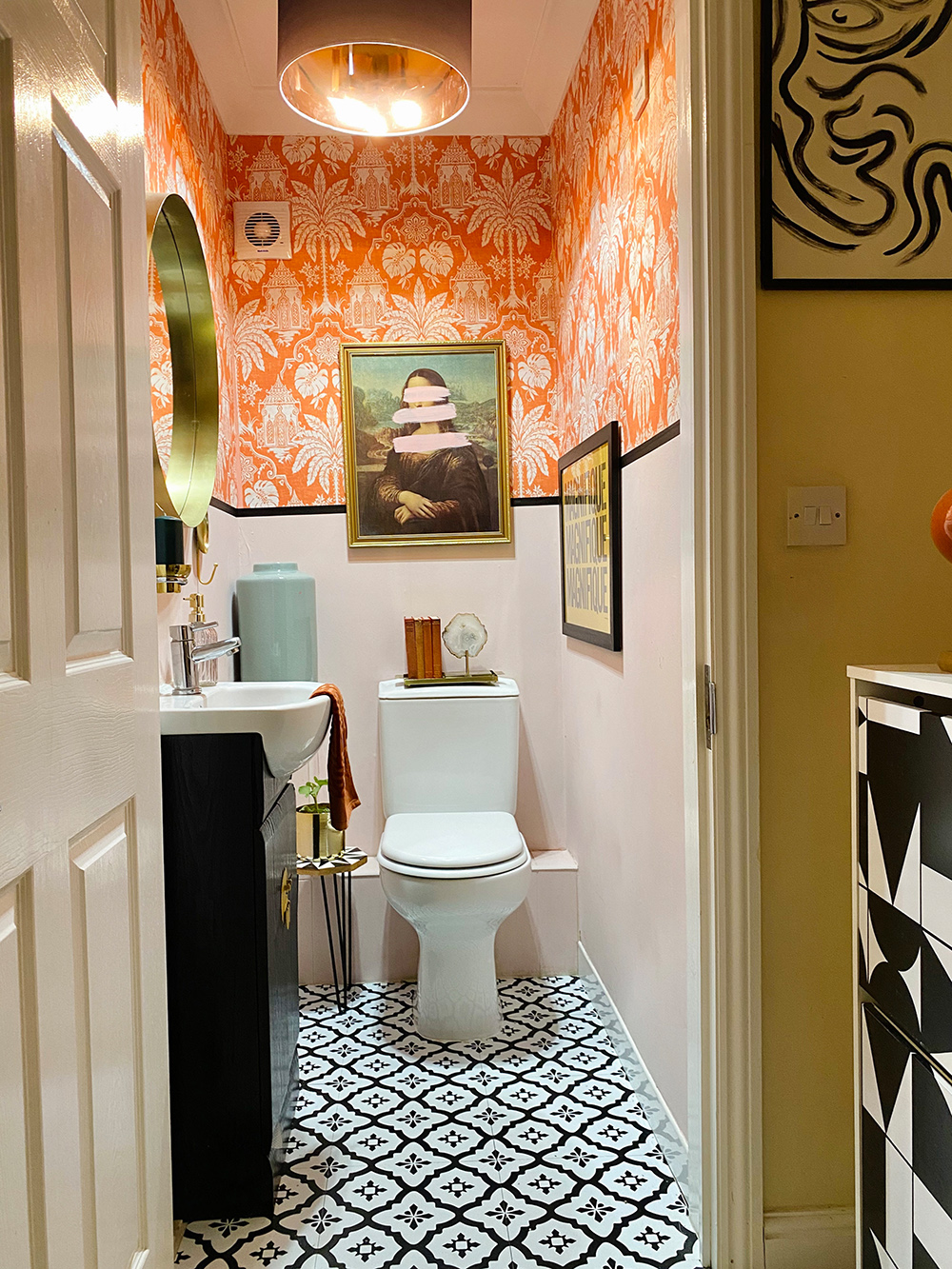 Gorgeous downstairs loo with with orange patterned wallpaper and monochrome patterned floor tiles.