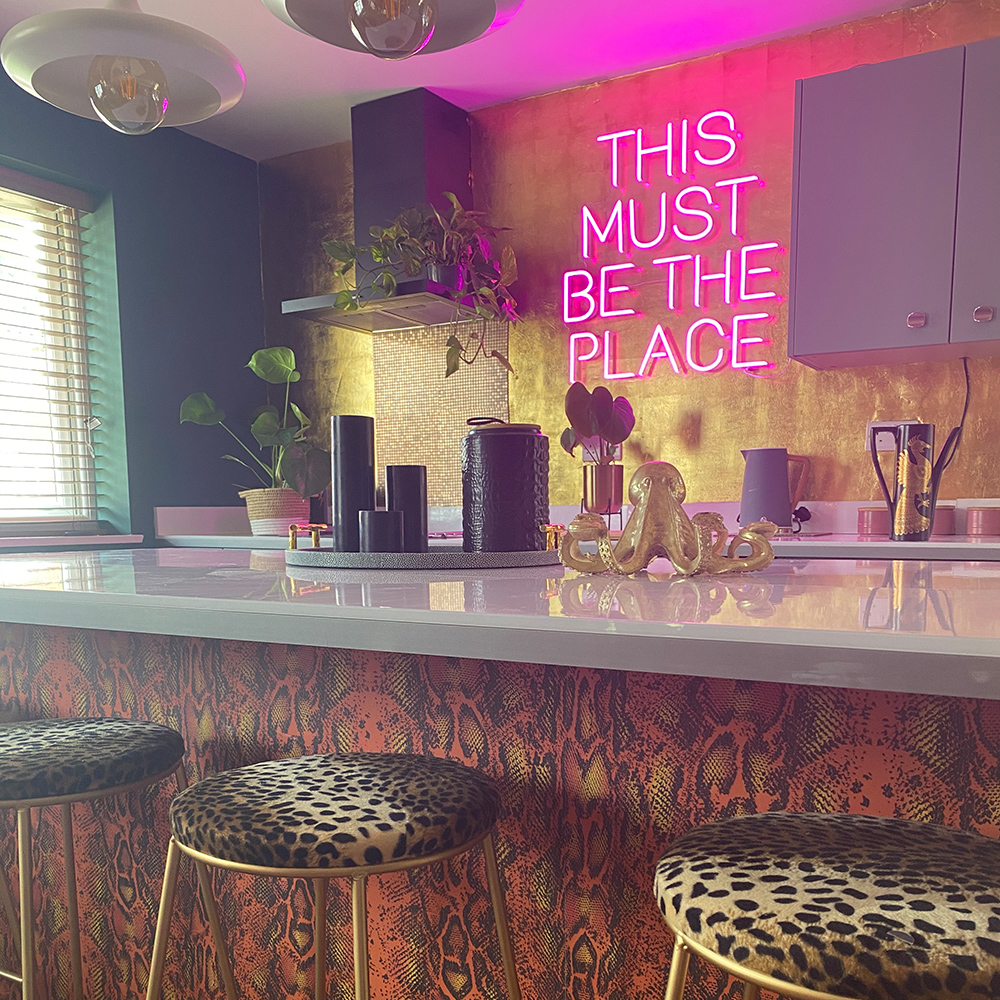 Eclectic kitchen design with This Must Be The Place pink peon sign. We love the clashing leopard print bar stools and snakeskin wallpaper. Image @inside.number.twelve