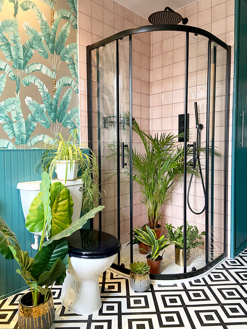 Tropical bathroom decor in pink and teal colours. Pink bathroom tiles with black shower cabinet and tropical wallpaper