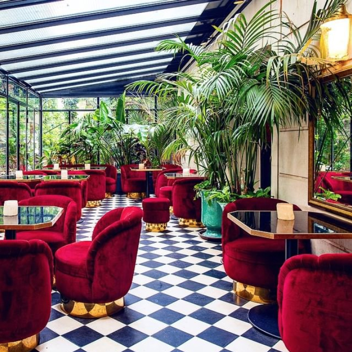 Stunning conservatory with black and white flooring, red velvet chairs and an abundance of tropical house plants