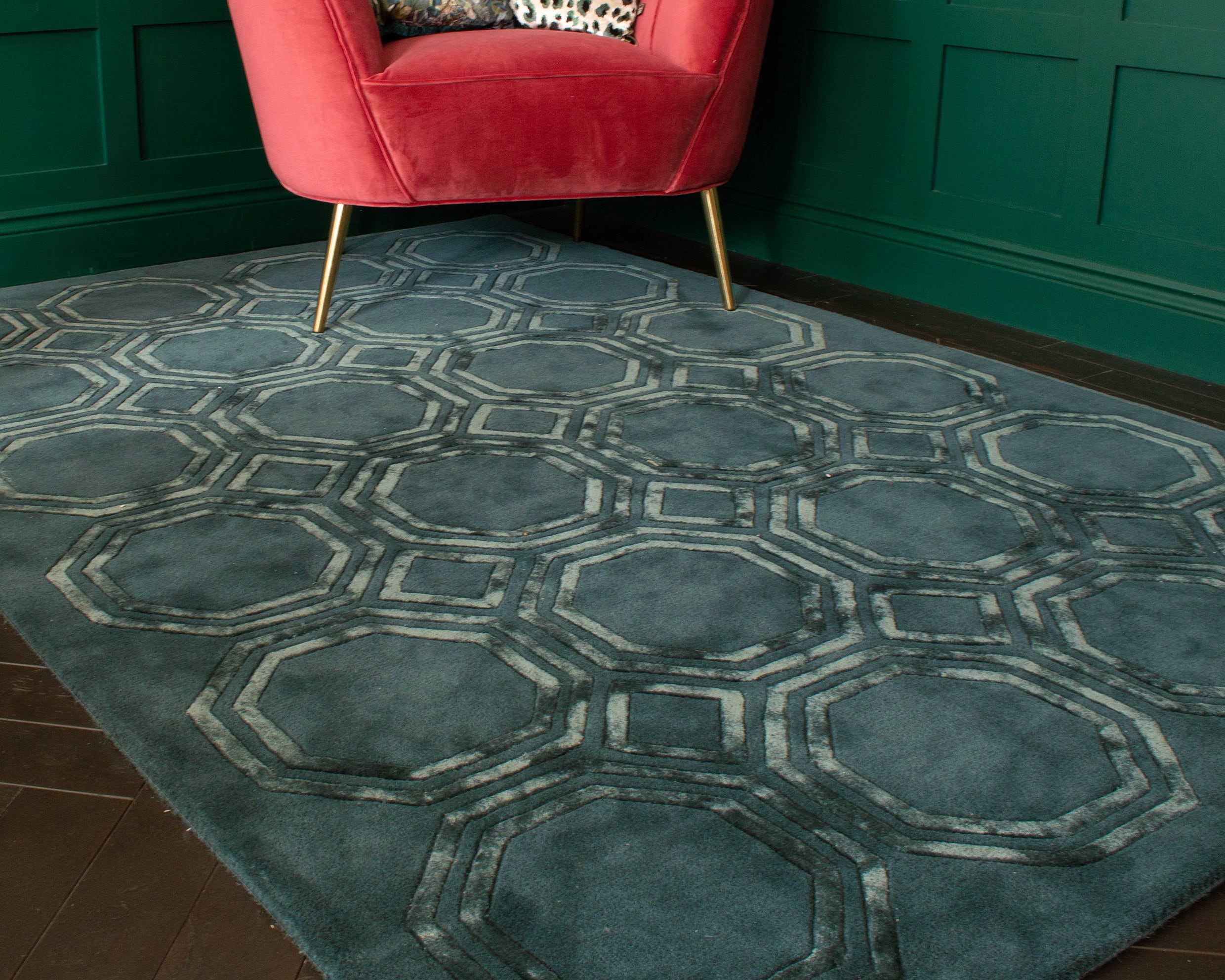 A teal-colored rug with a geometric pattern on a dark wood floor