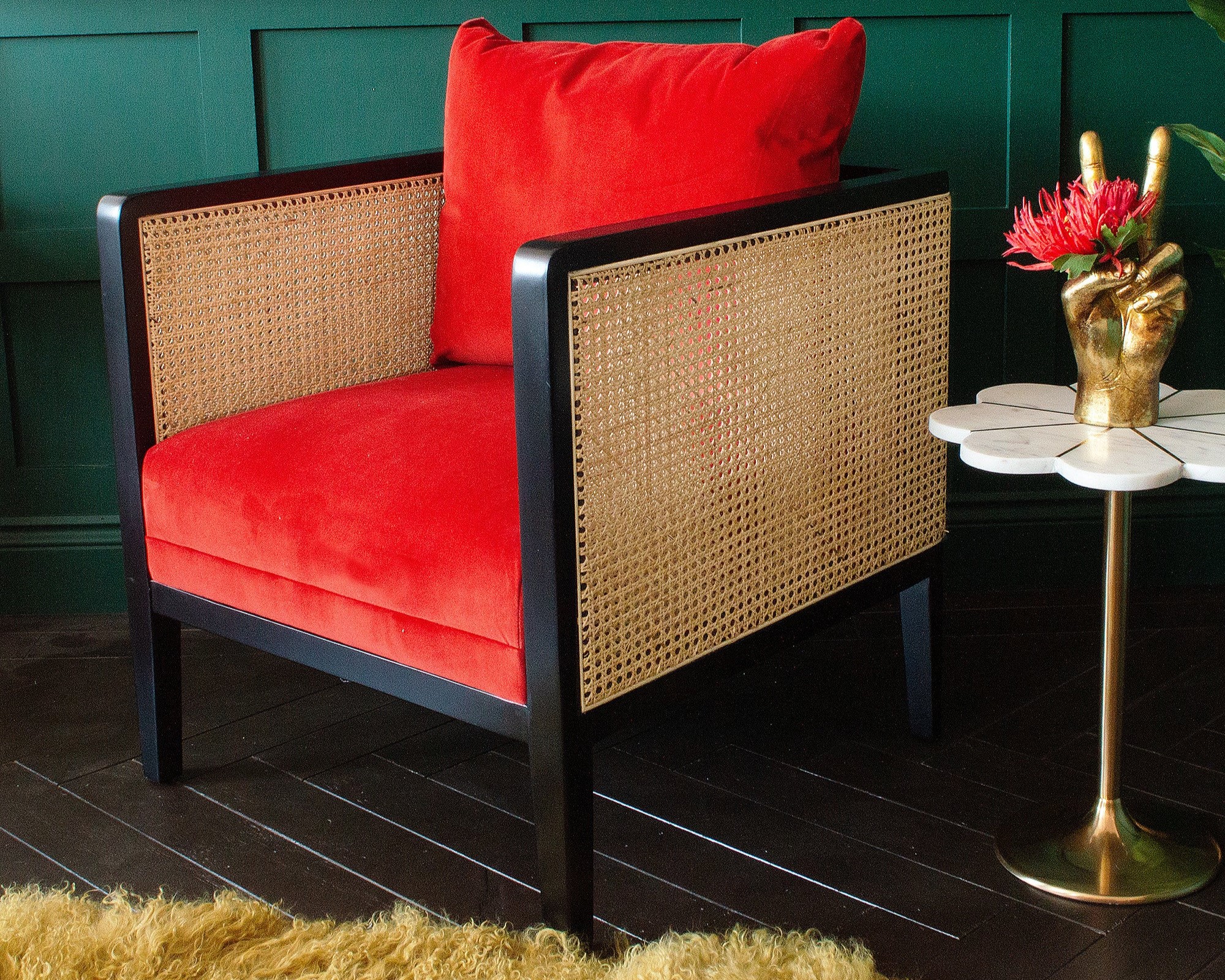 A red velvet rattan armchair with a black frame next to a side table