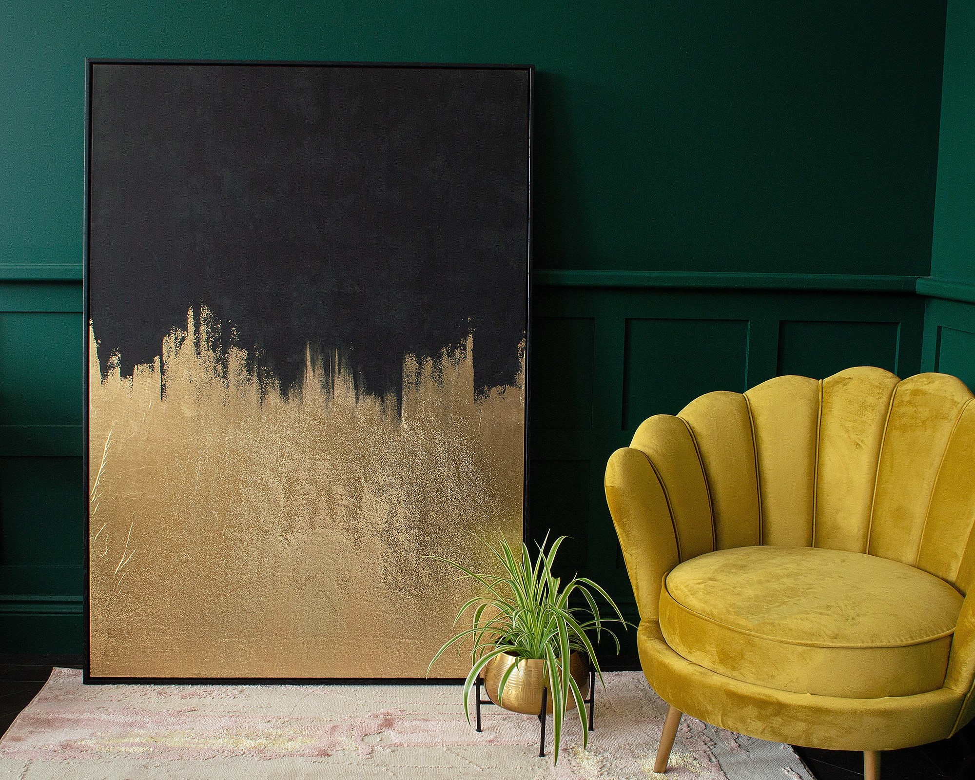 A black and gold abstract painting resting against a green wall next to a yellow velvet armchair