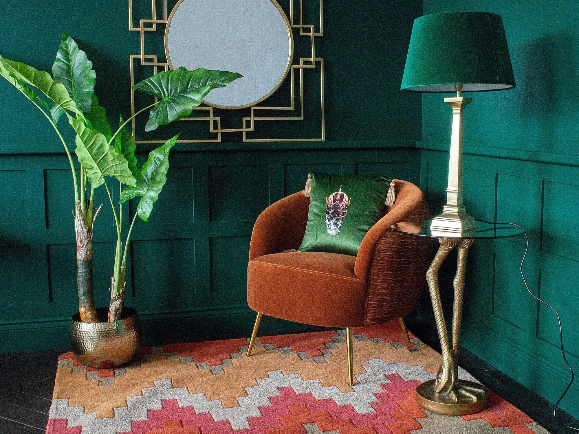 An orange armchair with a green cushion, and a tall green lamp next to it on a colourful rug