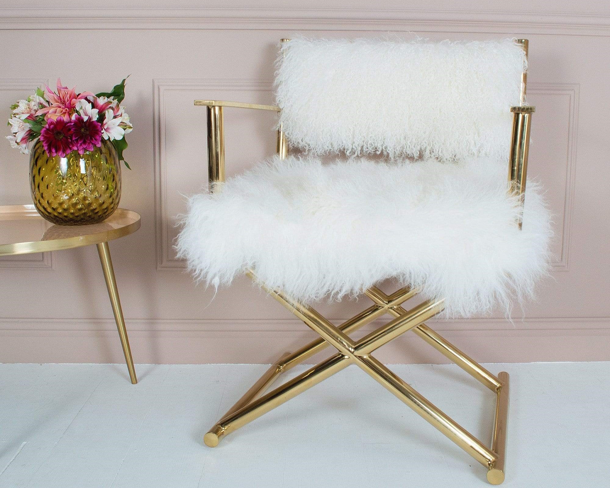 A gold metal framed chair with white fur set against a gold side table and a vase of colorful flowers