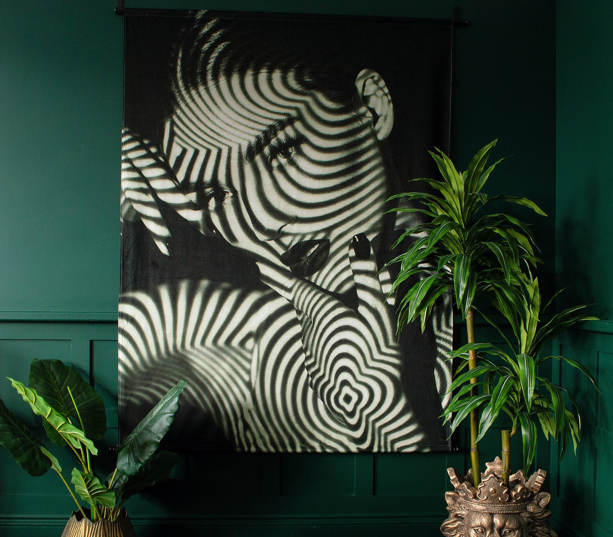 A black and white art piece of a woman's face with striped patterns hanging on a green wall