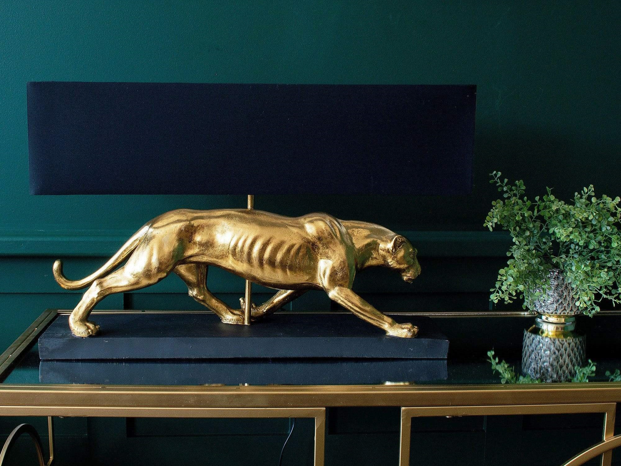 A golden sculpture of a Panther used as a base for a table lamp with a navy blue shade