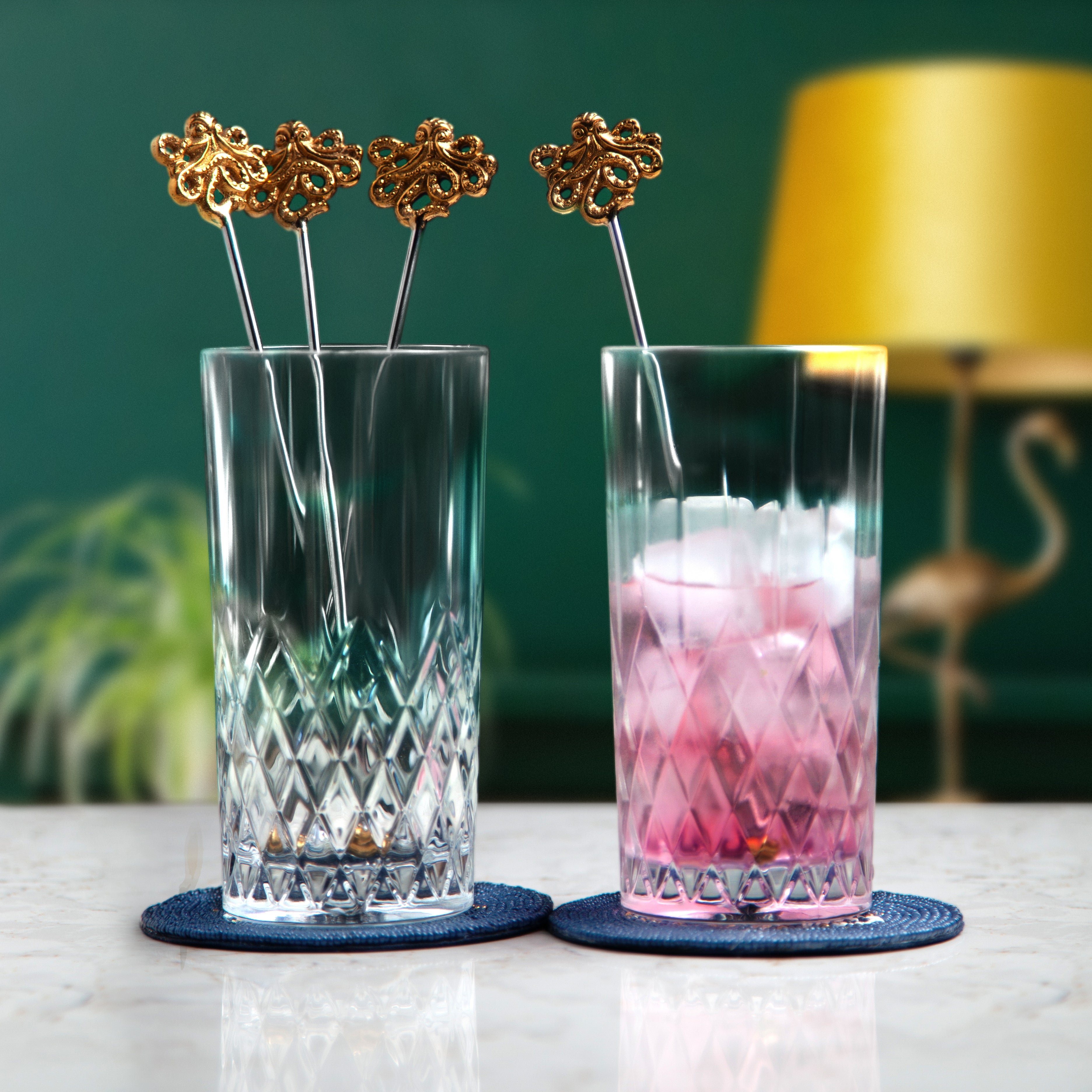 Gold octopus drink stirrers inside two glasses placed on drink coasters
