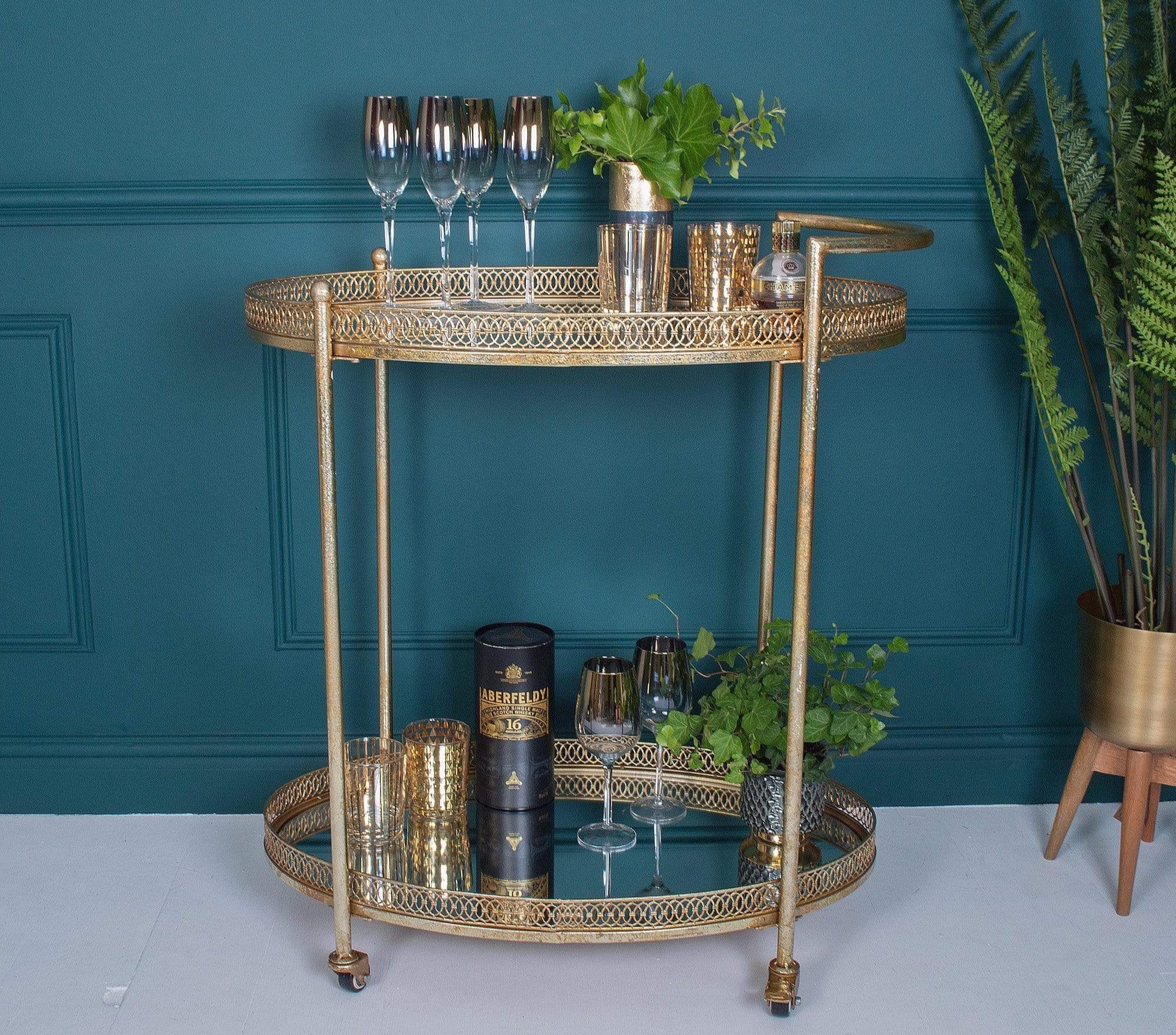 A gold metal bar cart with beautiful glassware and plant pots