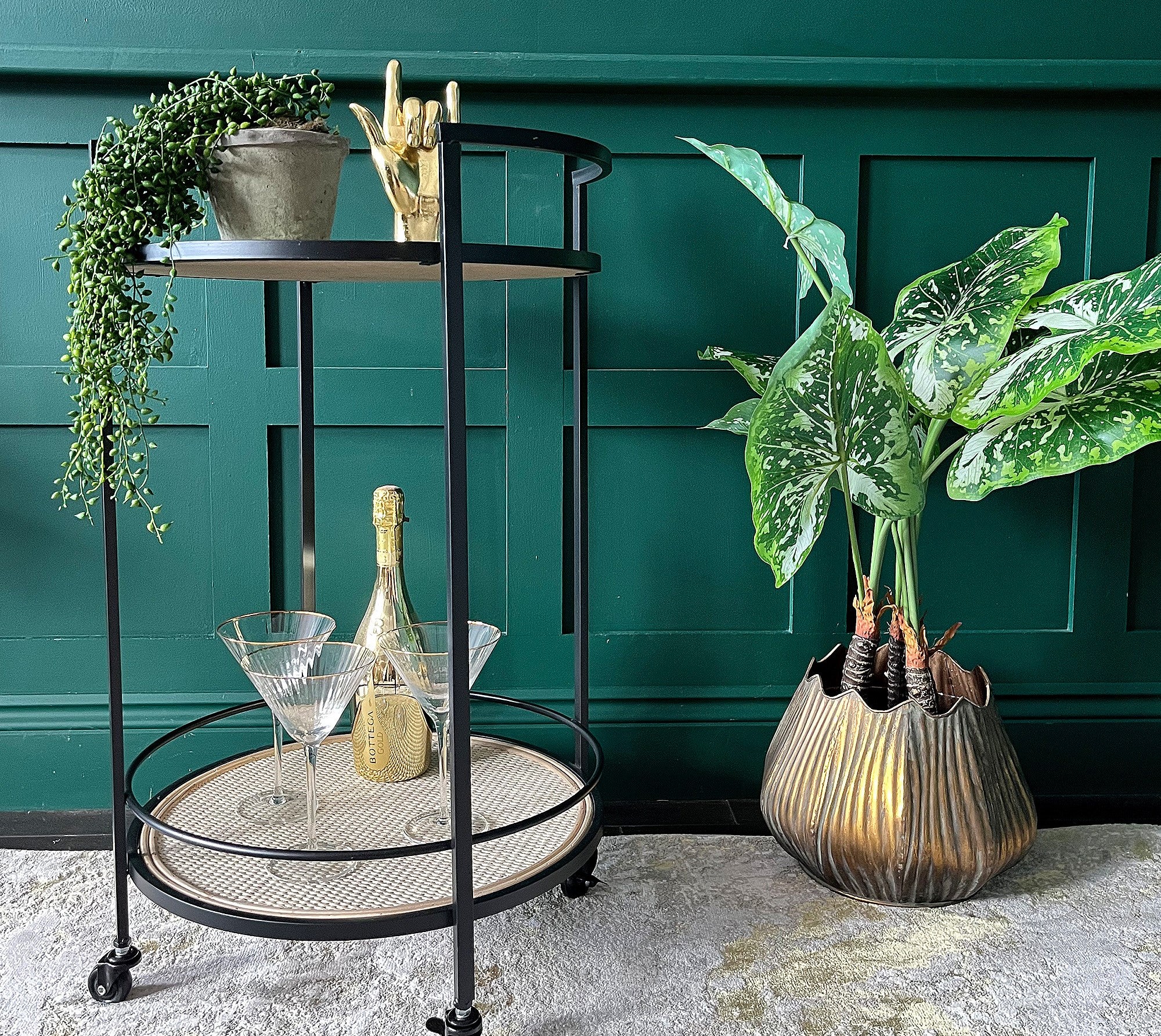 A black metal and rattan drinks trolley with glasses and plant pots