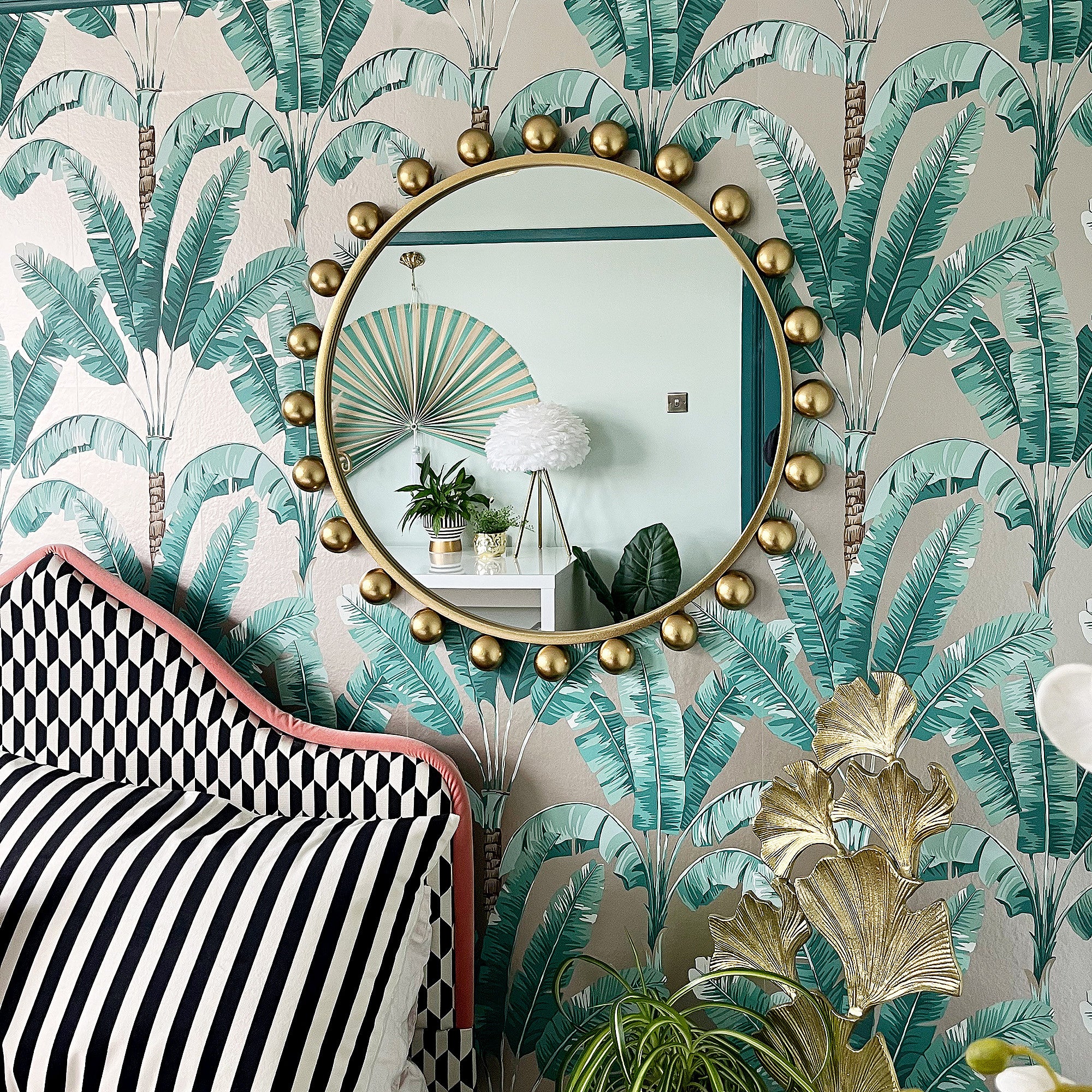 A round gold wall mirror next to a bed