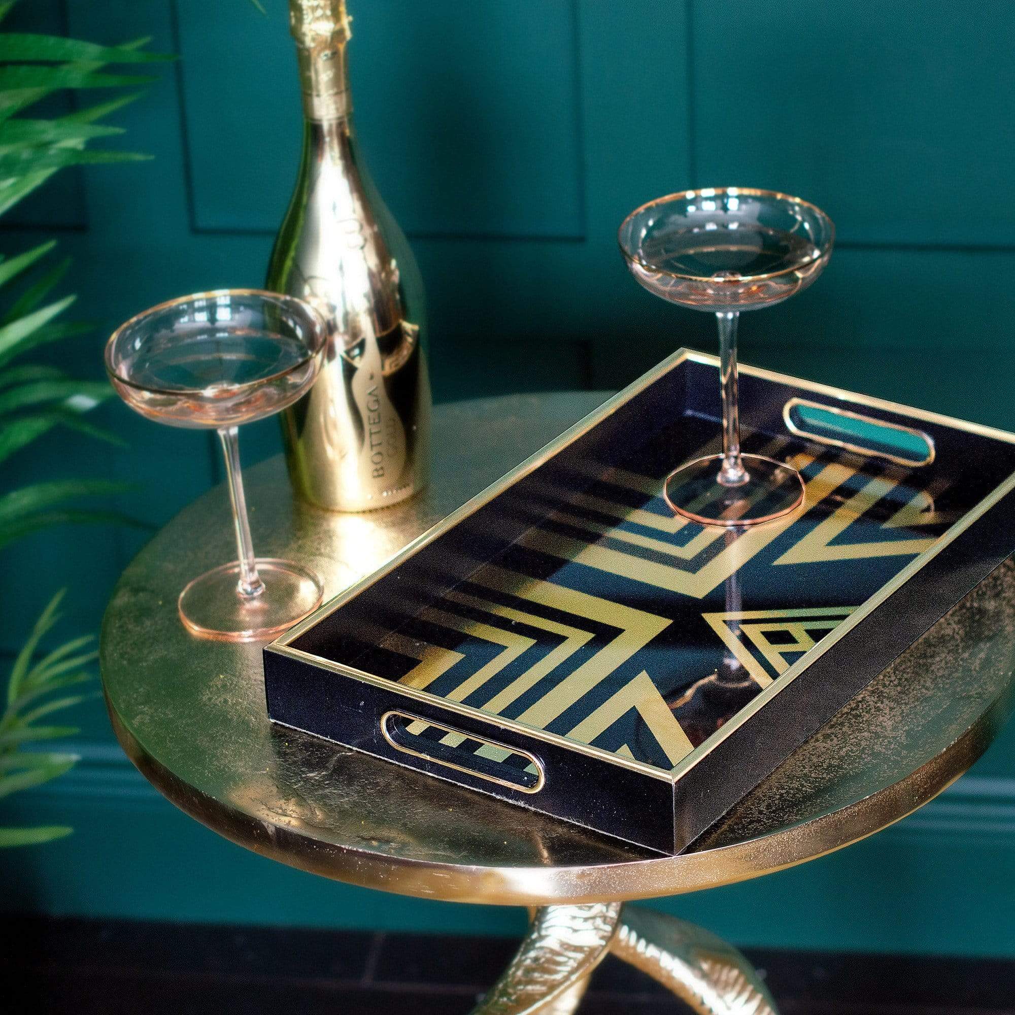 A black and gold tray with two glasses and a bottle placed on a top of a side table