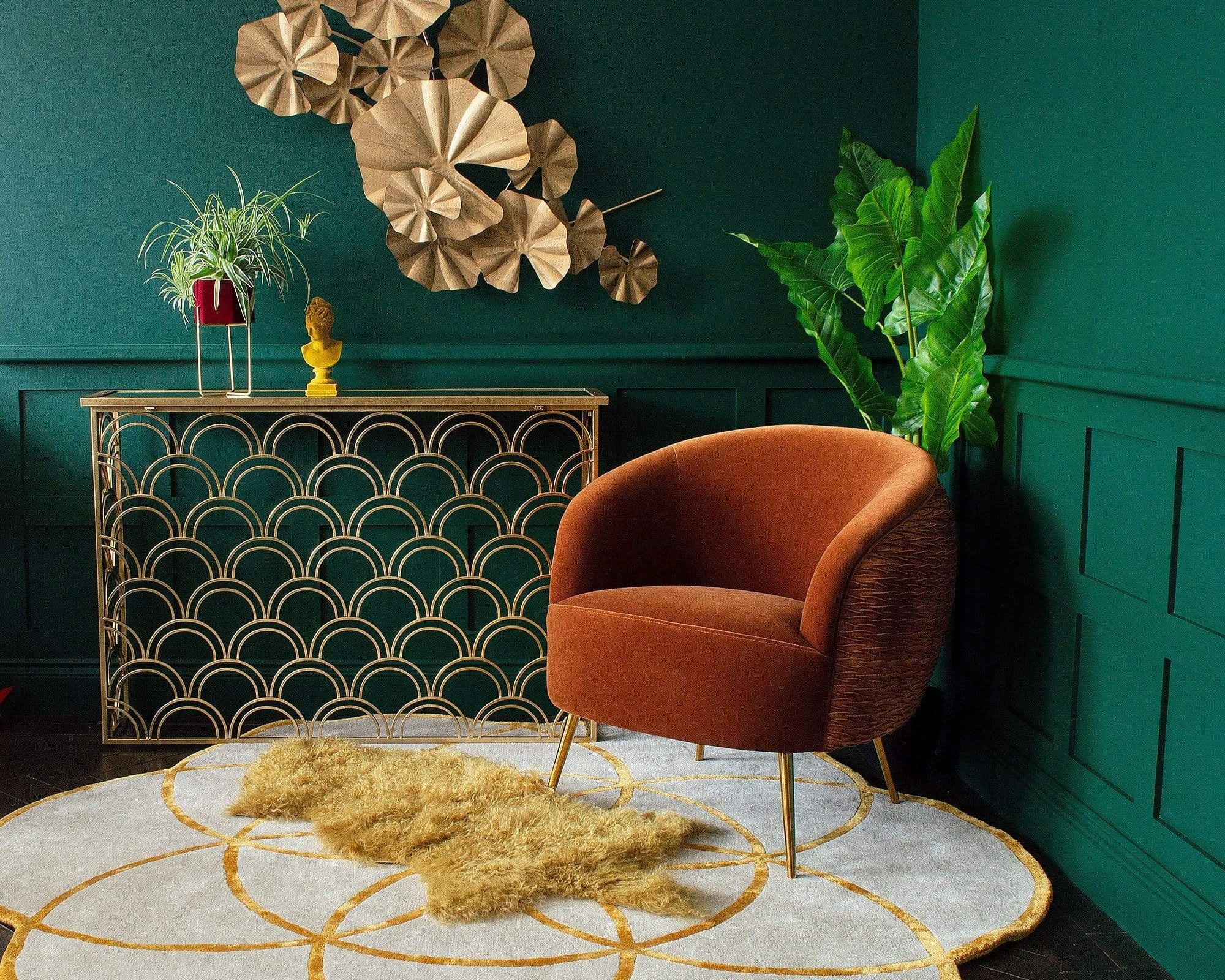An orange armchair next to a gold console table with plant pots and a rug