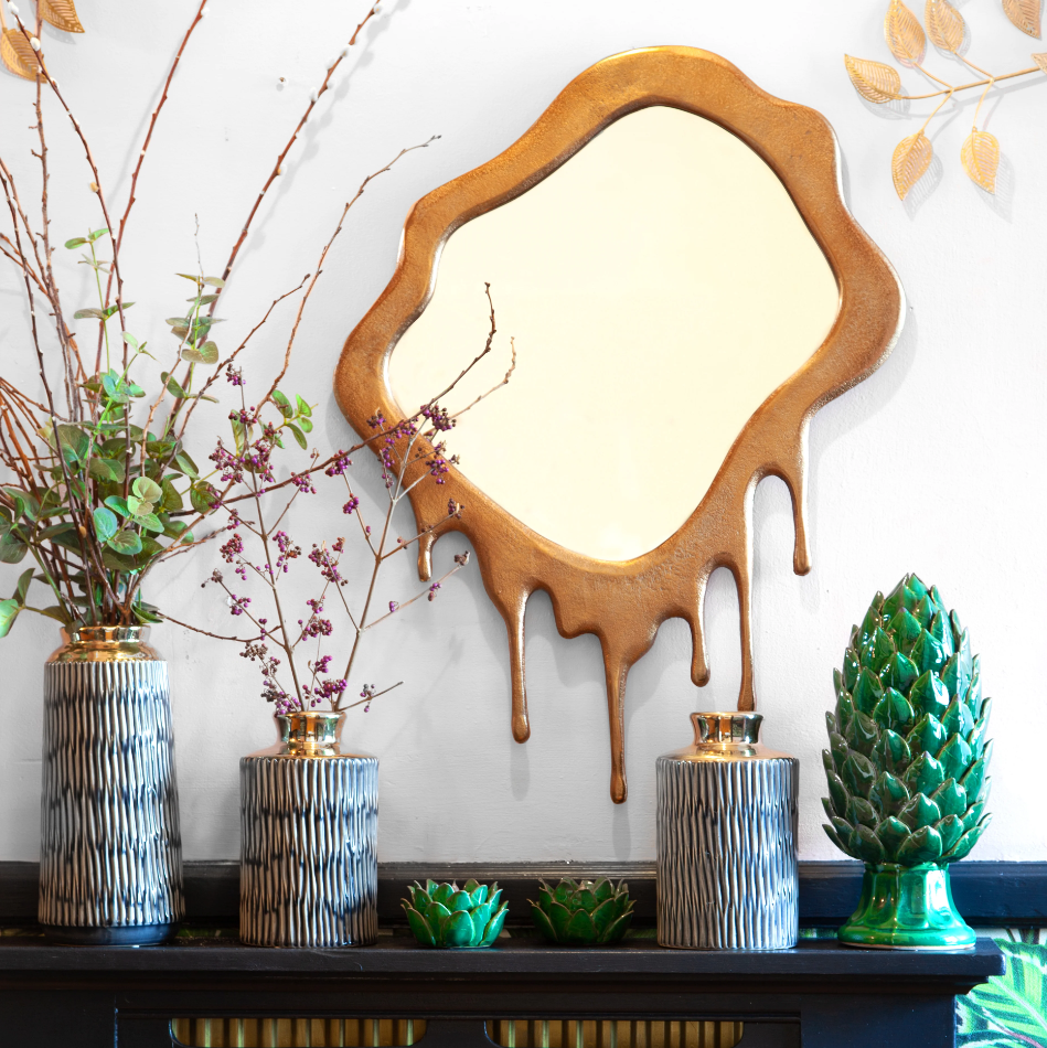 A dripping gold mirror on a wall and multiple flower vases