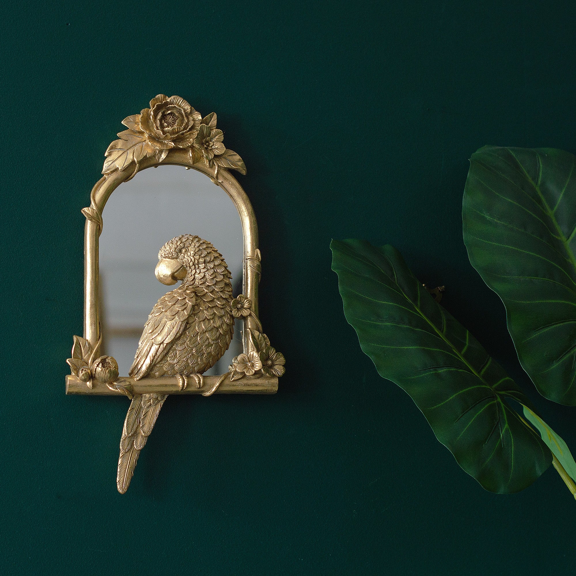 A golden perching parrot mirror on a green wall